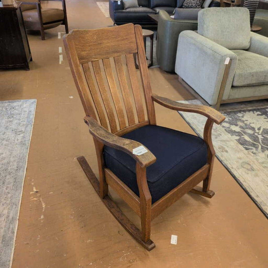 Wooden rocking chair with navy cushion on a brown floor, surrounded by furniture.