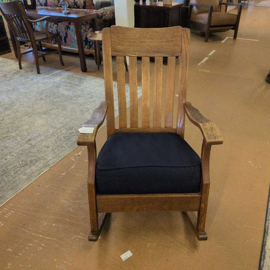 Wooden rocking chair with a black cushion on a brown floor.