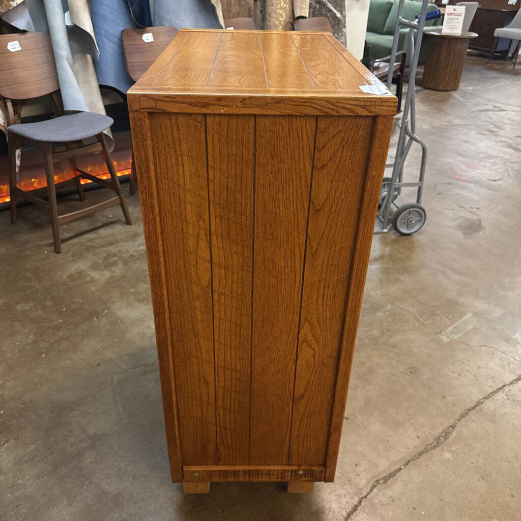 Wooden cabinet in a warehouse setting with other furniture items in the background.