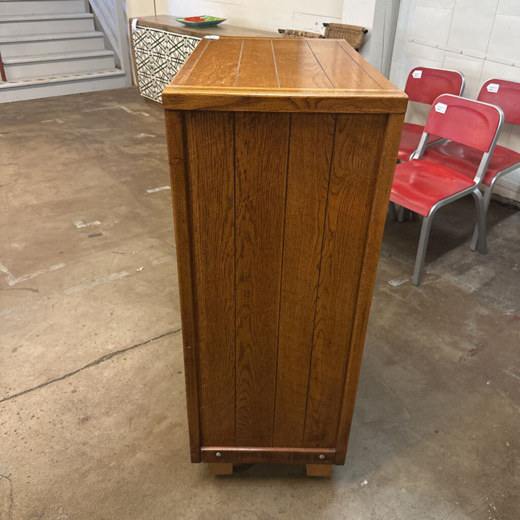 Wooden cabinet on a concrete floor with red chairs in the background
