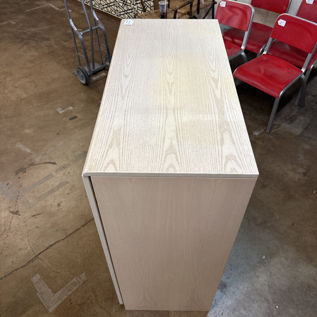 Wooden counter or reception desk in an indoor setting with red chairs and a dolly in the background.