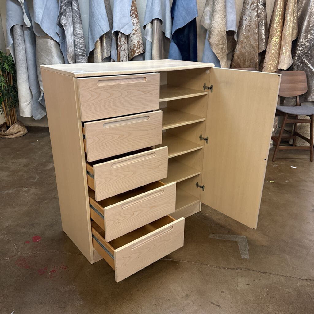 Wooden dresser with open door and multiple drawers in a room with clothing racks.