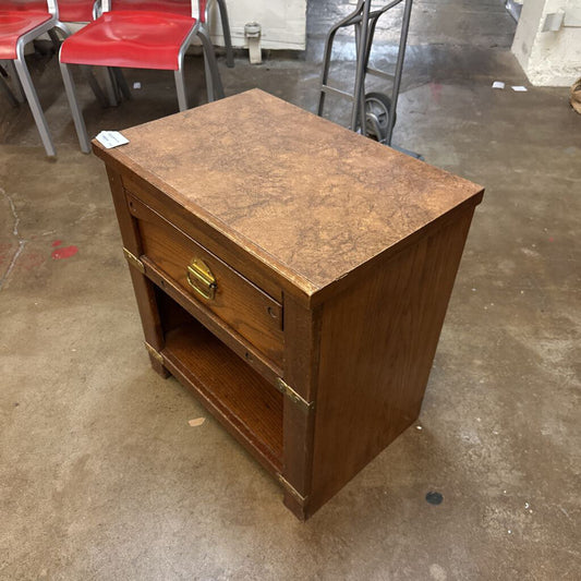 Wooden side table with a single drawer on a concrete floor.