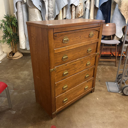 Wooden dresser with brass handles in a storage or warehouse setting