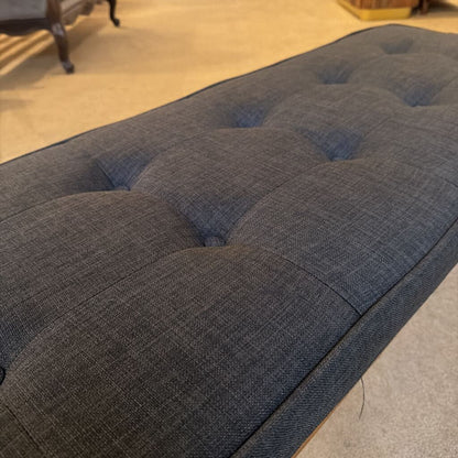 Gray upholstered bench with tufted design on a carpeted floor.