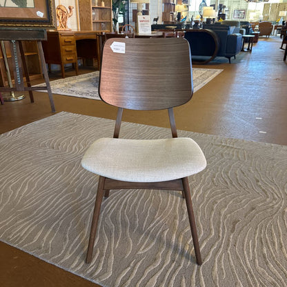 Wooden chair with beige cushion on a patterned rug in a store setting