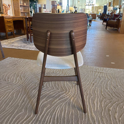 Wooden chair with a white seat on a textured carpet in a furniture store.