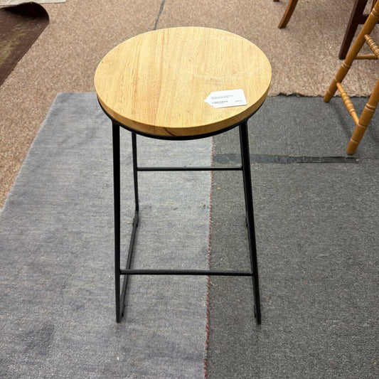 Wooden stool with black metal legs on a gray carpet