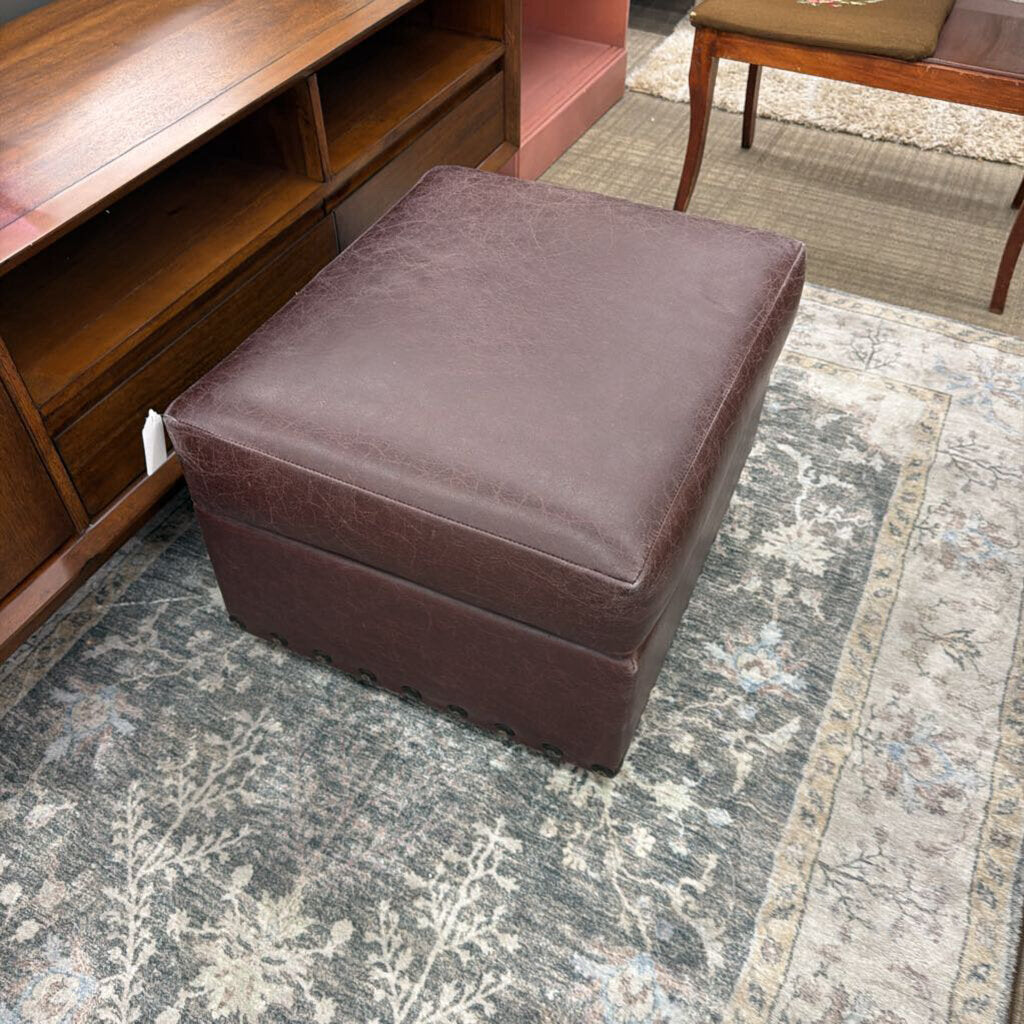 Brown ottoman on a patterned rug with wooden furniture in the background