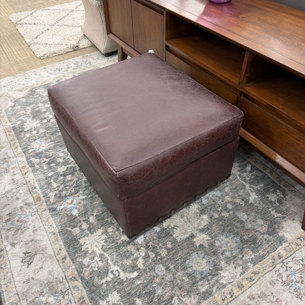 Brown leather ottoman on a patterned rug next to a wooden cabinet.