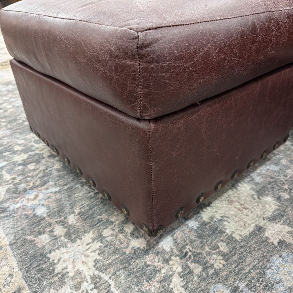 Brown leather ottoman on a textured gray floor