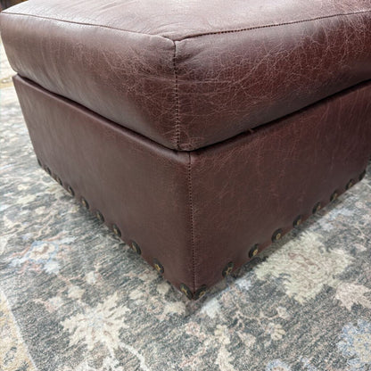 Brown leather ottoman on a textured gray floor
