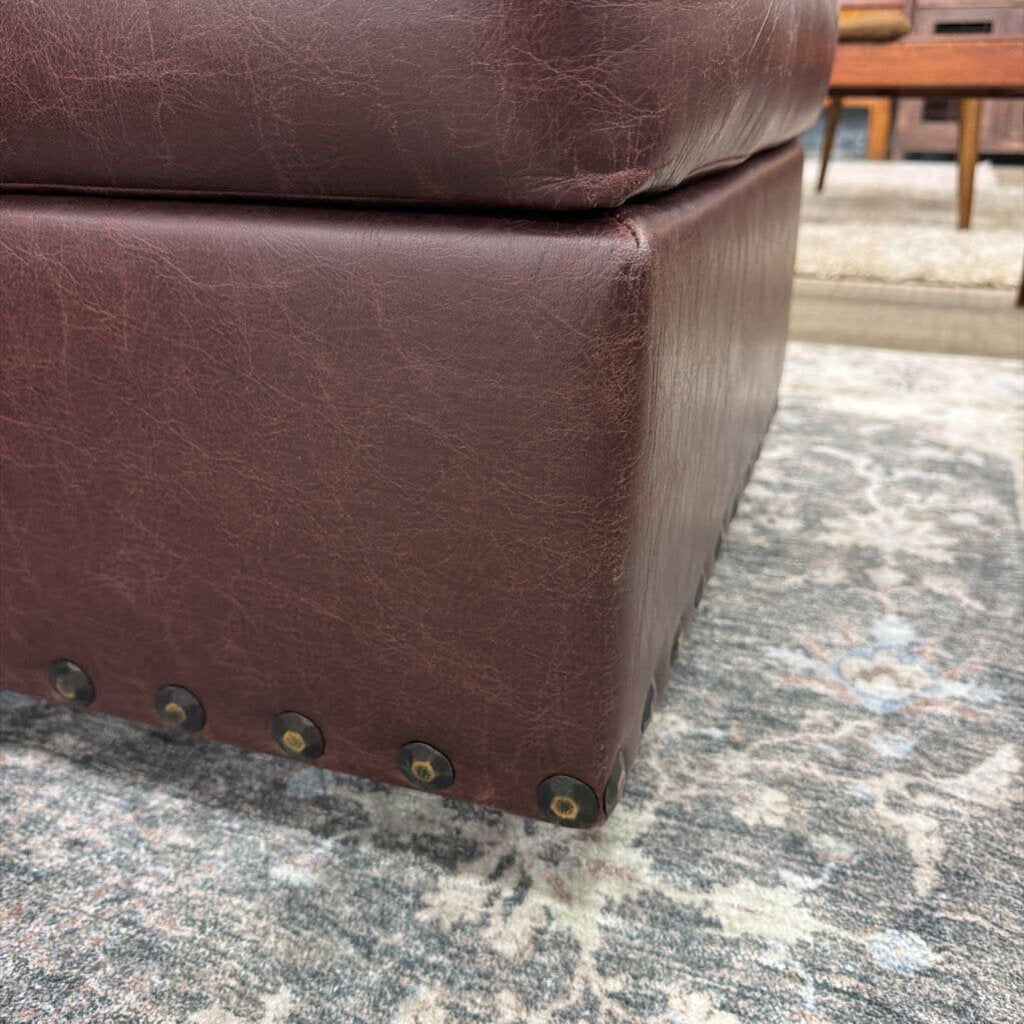 Brown leather ottoman with visible wear on a textured surface