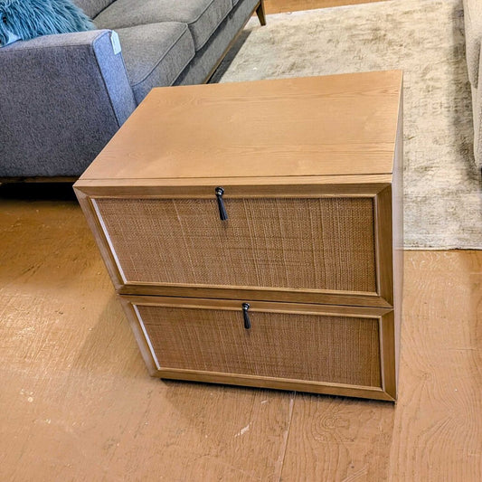 Wooden nightstand with wicker drawers on a wooden floor.
