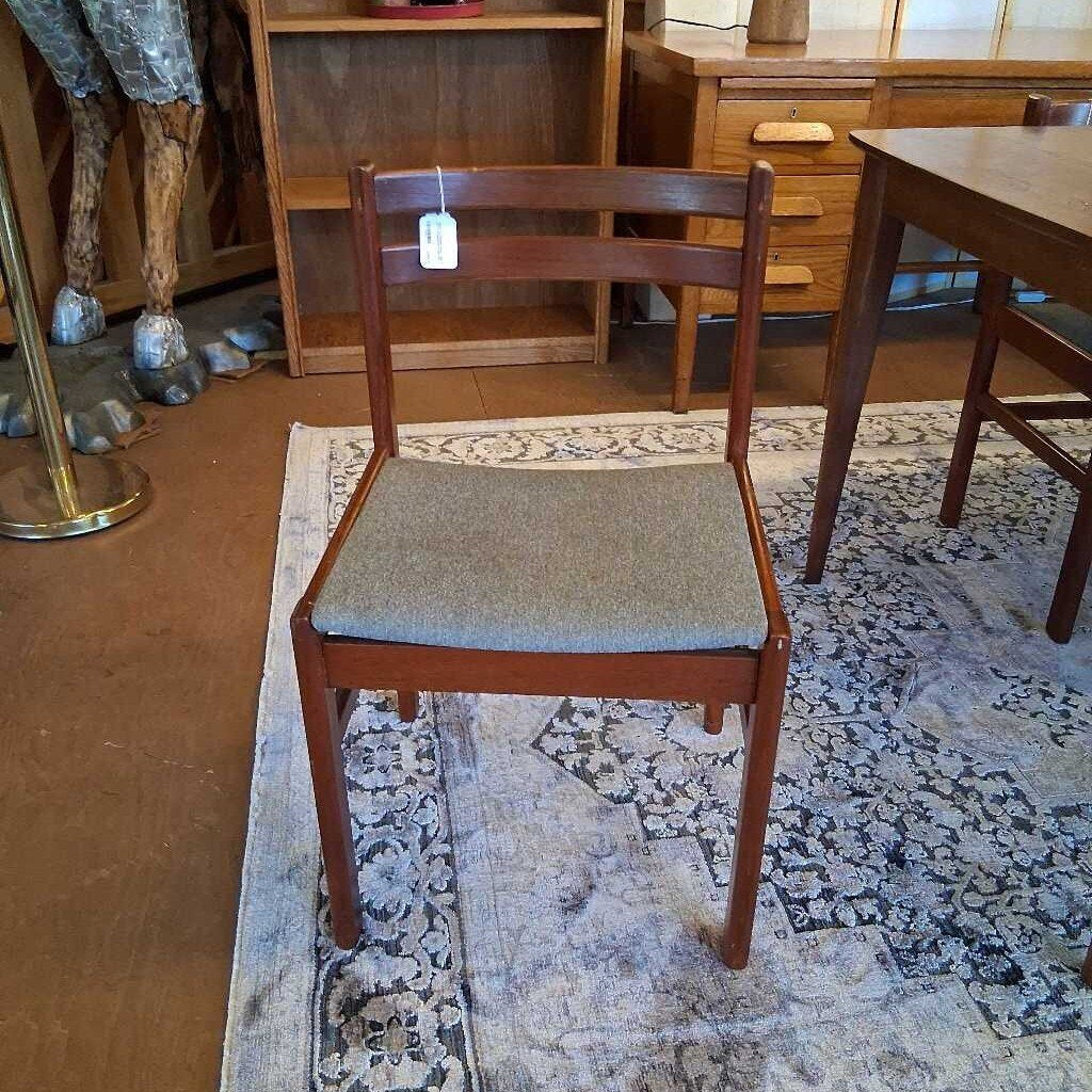 Wooden chair with a gray cushion on a patterned rug in a room with furniture.