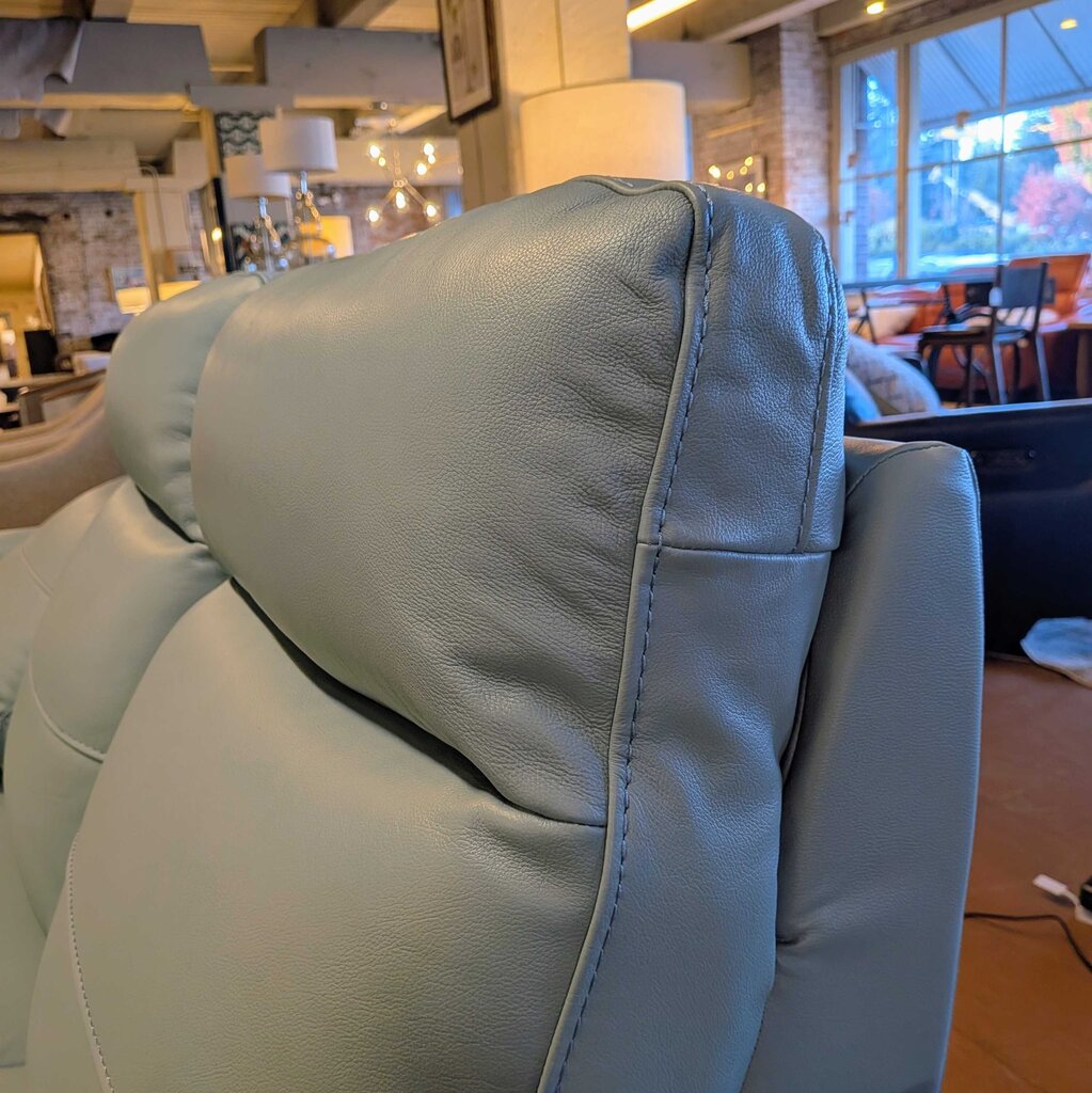 Close-up of a light gray leather armchair with a blurred indoor background