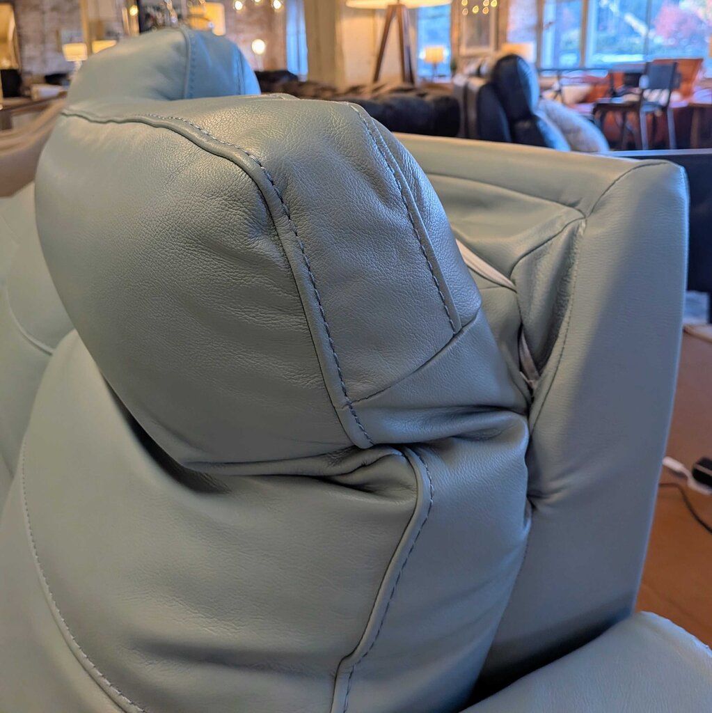 Close-up of a light gray leather chair with visible stitching in an indoor setting.