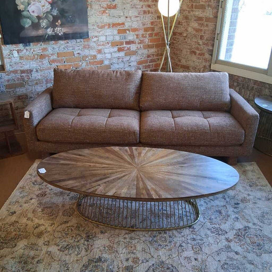 Brown sofa in a room with a brick wall and round wooden coffee table.