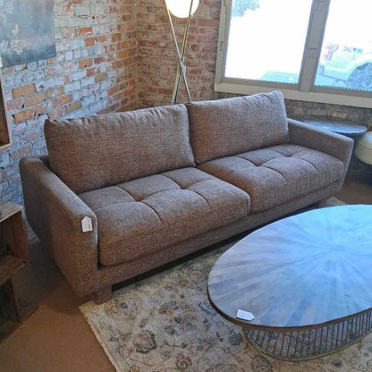 Brown sofa in a room with a brick wall and round glass table.