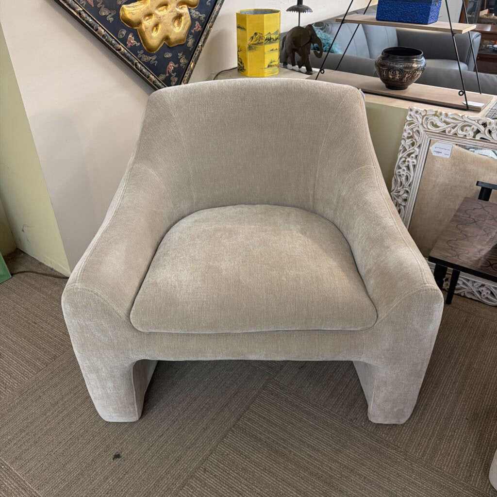 Beige armchair in a room with decor items on a shelf.
