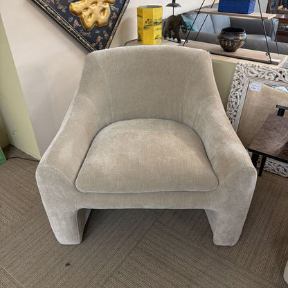 Beige armchair in a room with decor items on a shelf.