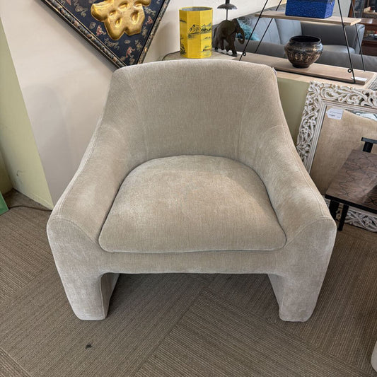 Beige armchair in a room with decor items on a shelf.