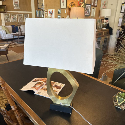 Lamp with a white shade on a table in a room with furniture and decor.