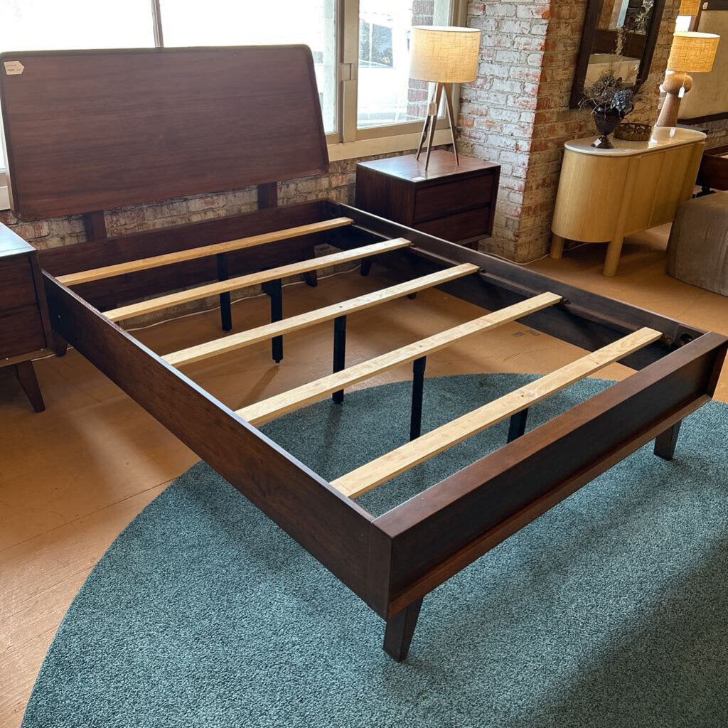 Wooden bed frame in a room with a rug and furniture.
