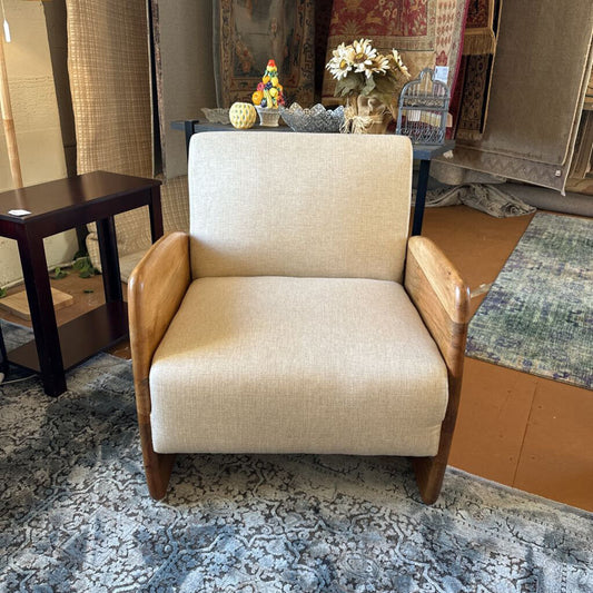 Beige armchair in a room with a rug and various items on a table.
