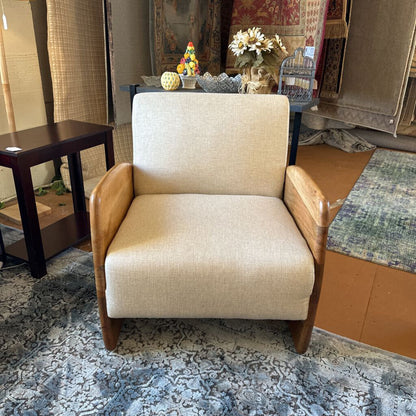 Beige armchair in a room with a rug and various items on a table.