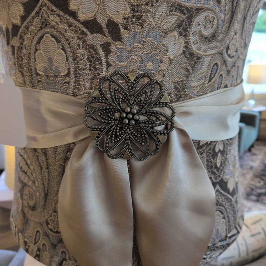 Decorative brooch on a dress with intricate patterns and a satin ribbon.