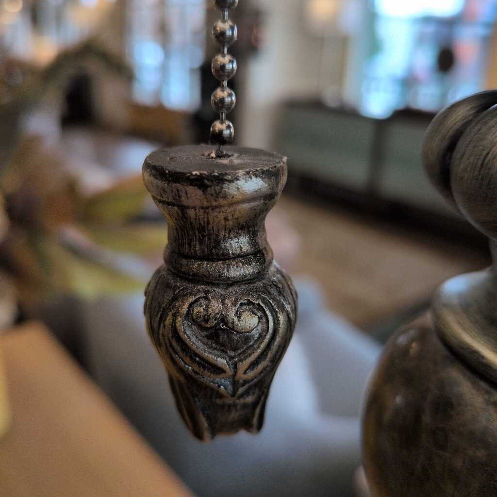 Decorative lamp pull chain with intricate design in a blurred indoor setting