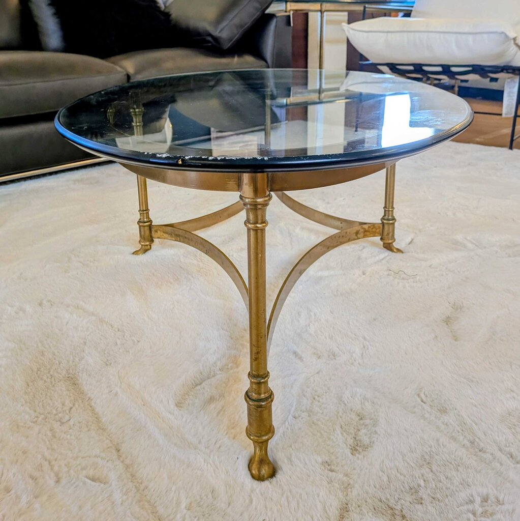 Round glass coffee table with gold metal legs on a white rug