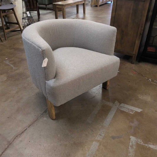 Gray armchair on a concrete floor with wooden furniture in the background