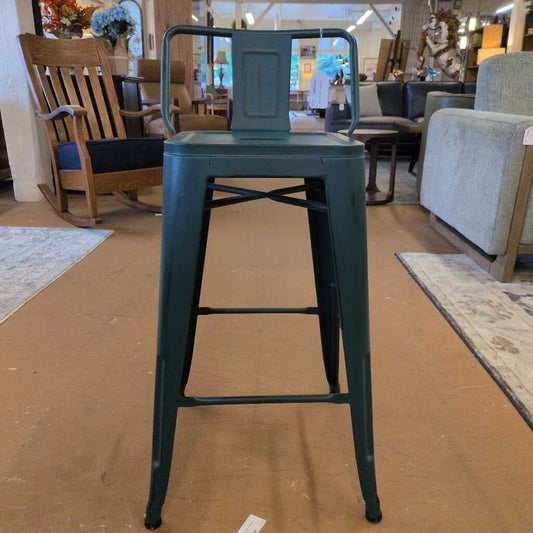 Green metal bar stool in a furniture store setting with chairs and tables in the background.