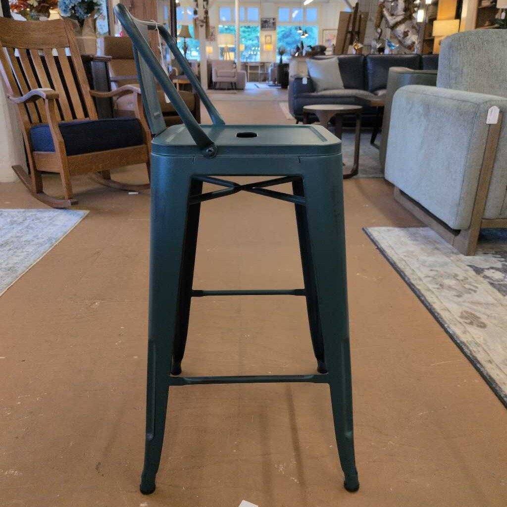 Green metal bar stool in a furniture store setting with chairs and tables in the background.