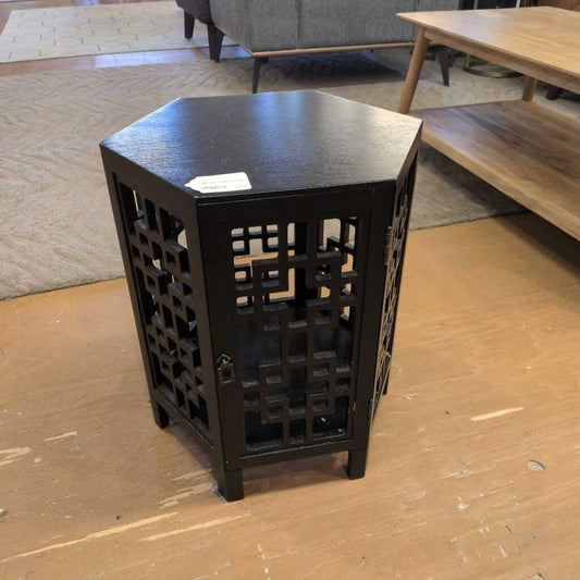Black hexagonal side table on a wooden floor with a blurred background