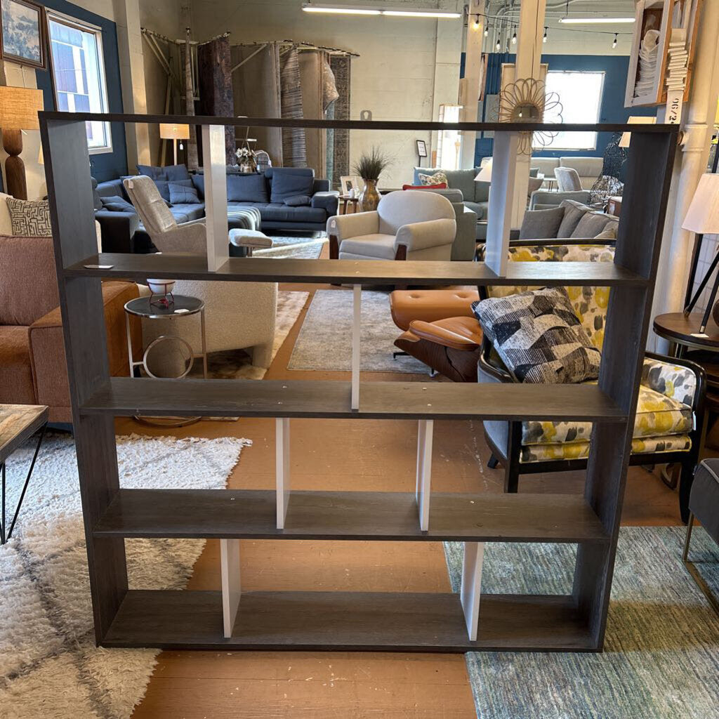Dark brown bookshelf in a furniture store with various seating arrangements in the background.