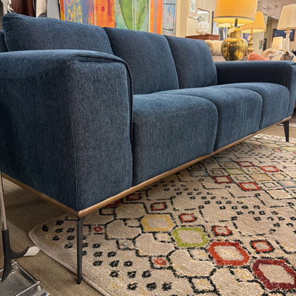 Blue sofa in a living room setting with a patterned rug and colorful artwork.