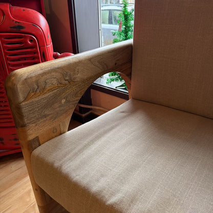Chair with wooden backrest and beige cushion in a room with a red vehicle and window in the background.