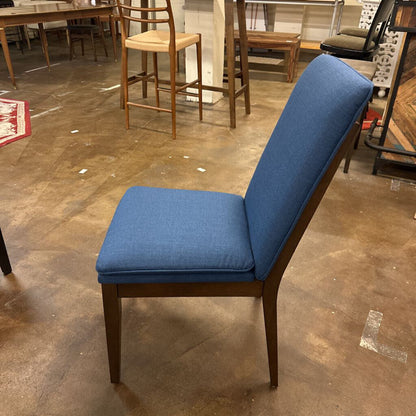 Blue cushioned chair on a concrete floor with other furniture in the background