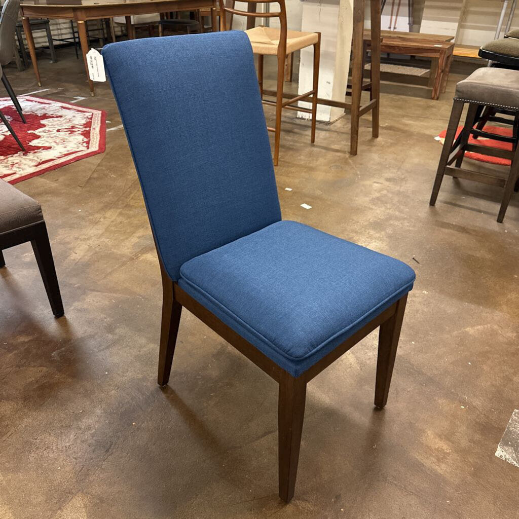 Blue upholstered chair on a concrete floor with other furniture in the background