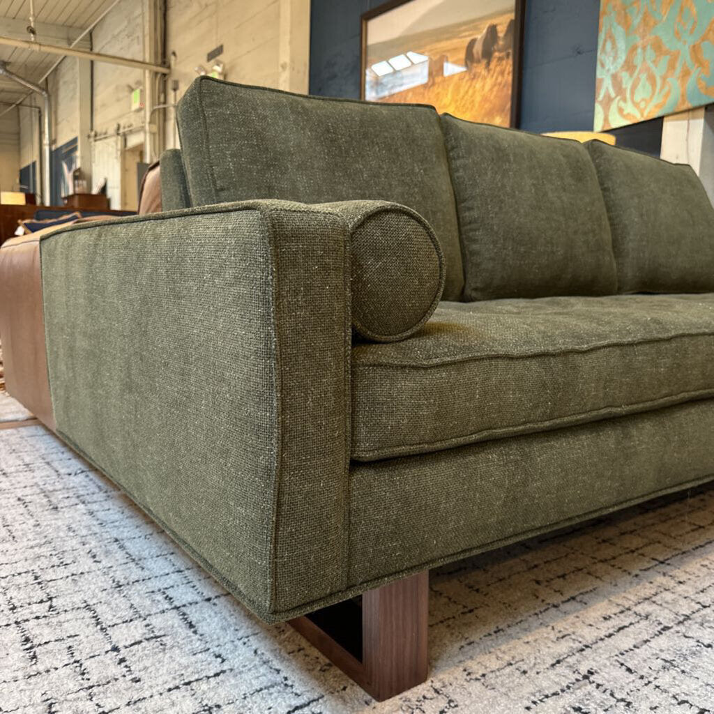 Green sofa in a room with a patterned rug and artwork on the wall.