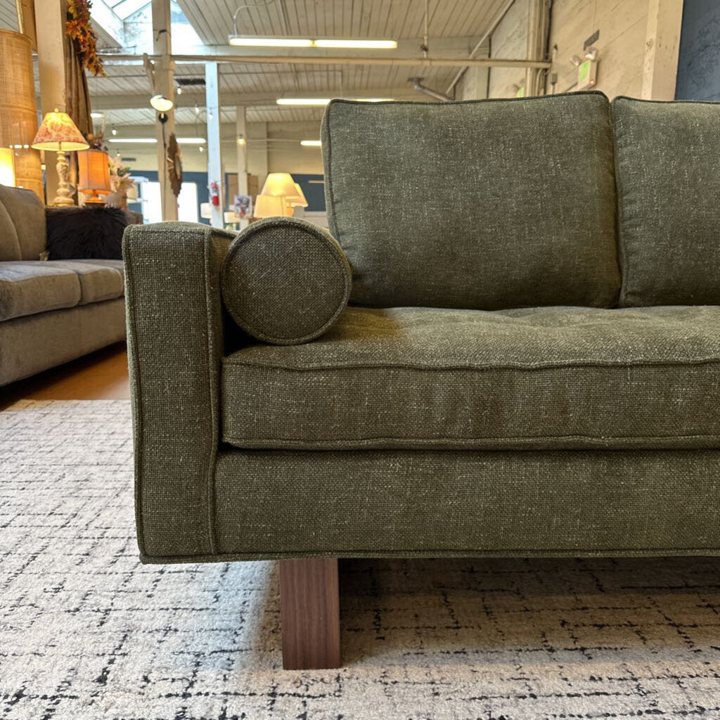 Green sofa in a store setting with other furniture and decor items.