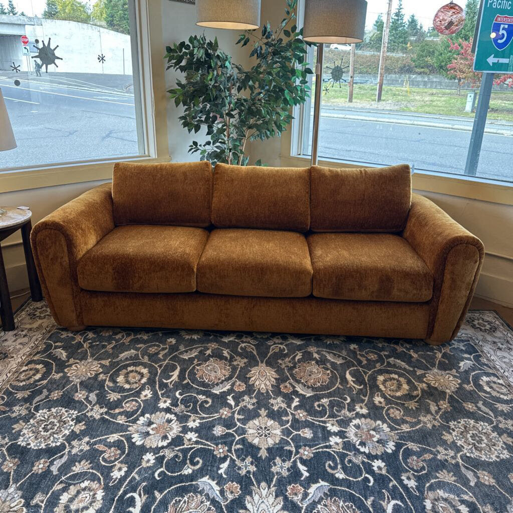 Brown sofa in a room with a patterned rug and large windows.