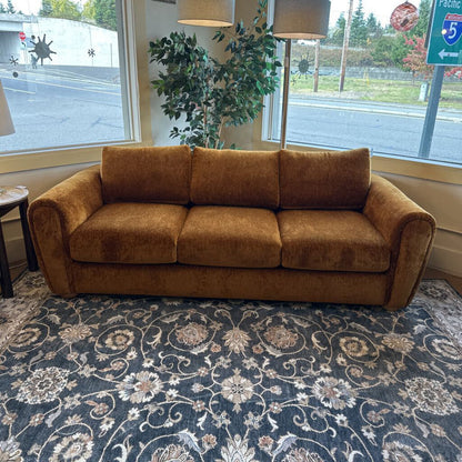 Brown sofa in a room with a patterned rug and large windows.
