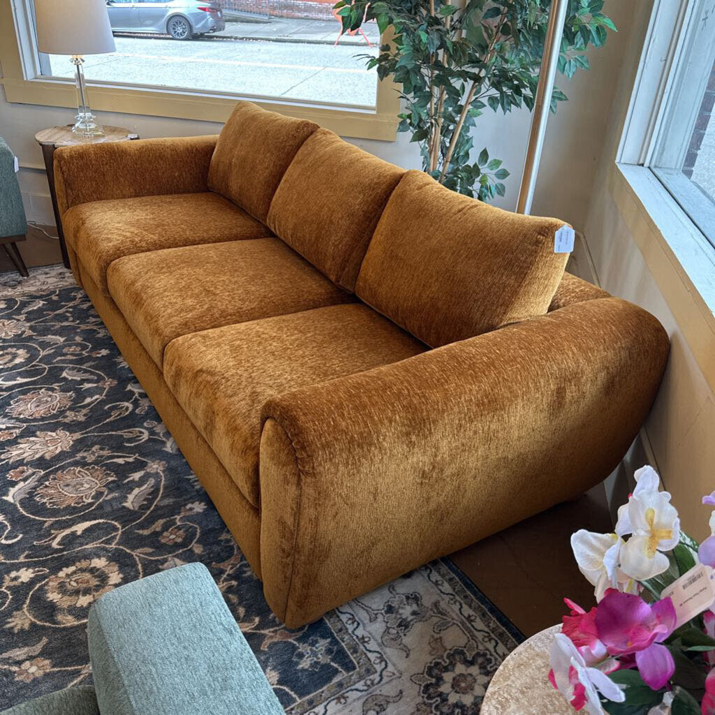 Brown sectional sofa in a room with a patterned rug and a plant.