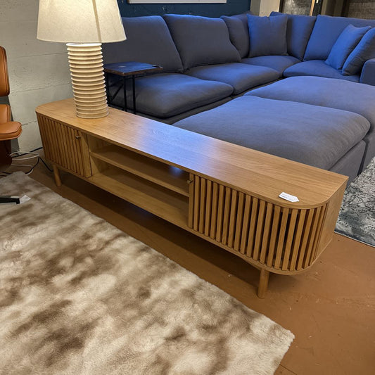 Wooden TV stand in front of a blue sectional sofa with a lamp on top.