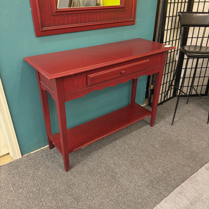 Red console table against a teal wall with a mirror above it.