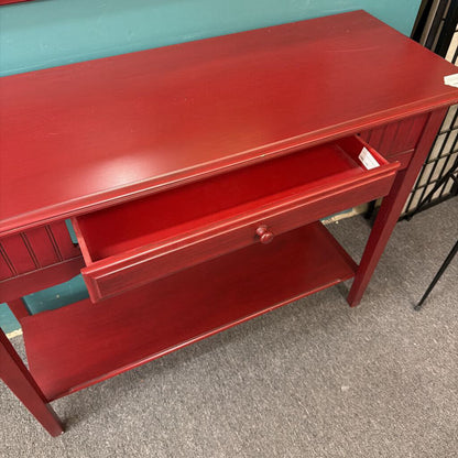 Red wooden desk with a drawer on a gray floor against a teal wall.